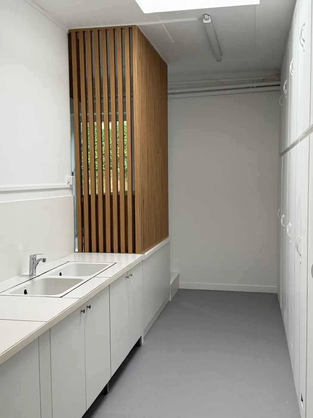 Point d'eau et rangements sous un claustra en bois, dans le laboratoire rénové