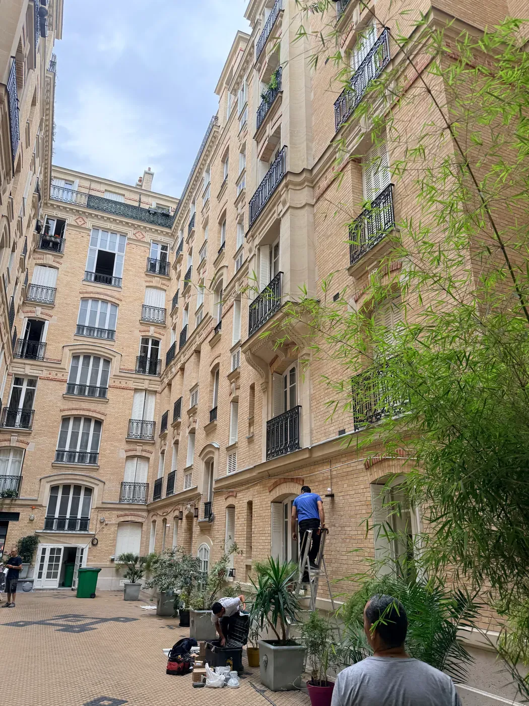 Électricien sur escabeau posant un cheminement électrique le long de la façade sur cour