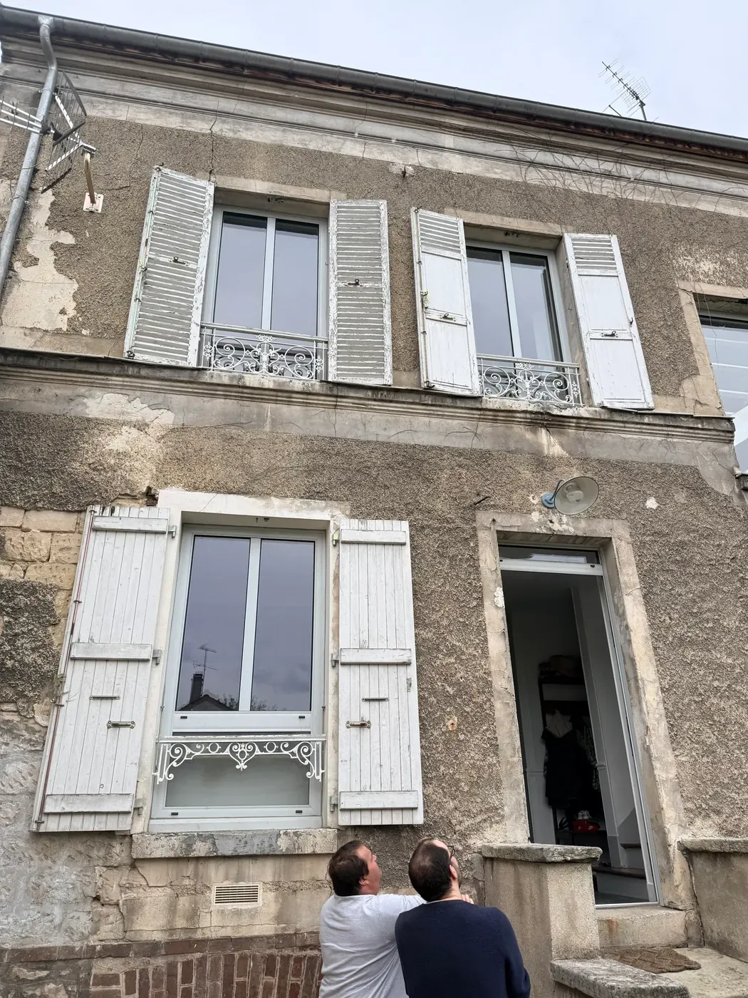 La même façade avant travaux : enduit décollé et moellons apparents sous les fenêtres à volets persiennés